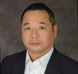 headshot of asian man with short black hair wearing a black blazer and white collared shirt