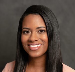 headshot of a black woman with long brown hair smiling in a pink blazer